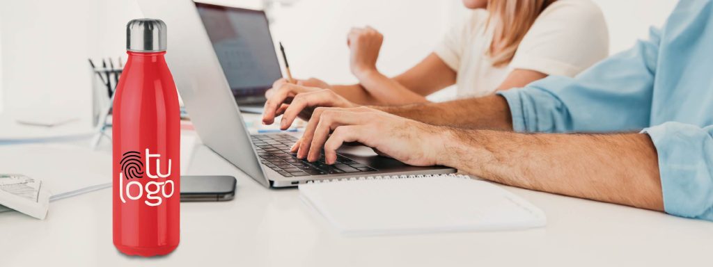 hombre trabajando en su portátil con una botella personalizada en el escritorio
